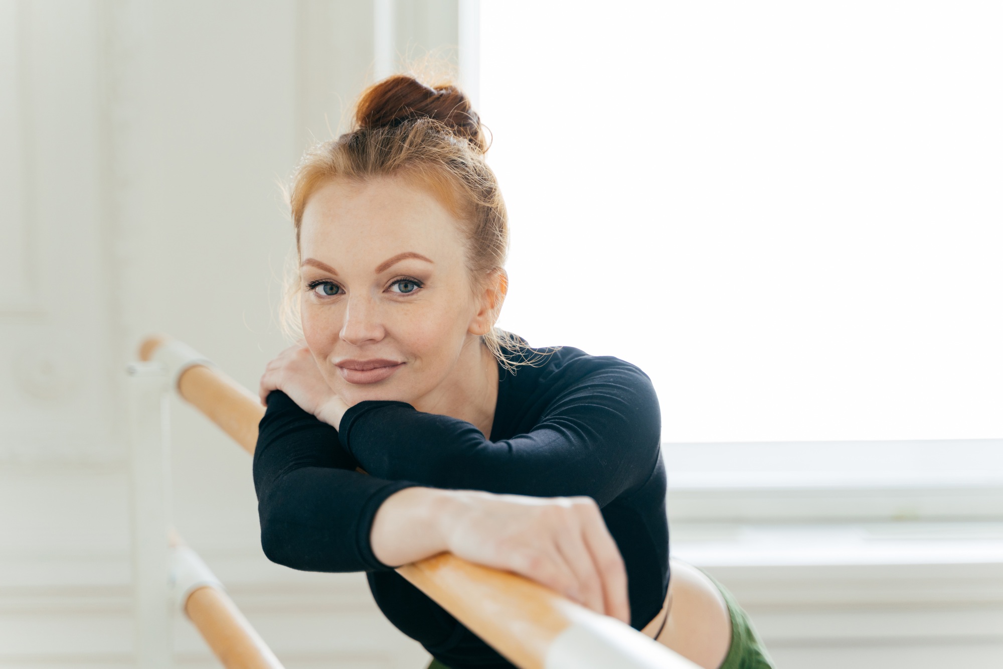 Headshot of calm beautiful female ballet dancer with ginger bun, wears sportswear